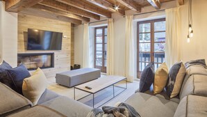 Een moderne woonkamer met een houten plafond, een grote flatscreen televisie, een grijze bank en een salontafel.