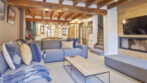 Een moderne woonkamer met een houten plafond, een grijze bank, een houten salontafel en een groot televisiescherm.