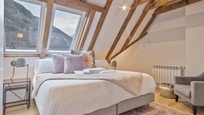 Een slaapkamer met een groot bed, een bureau, een stoel, een raam met uitzicht op bergen en een radiator.