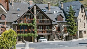 Een chalet in traditionele stijl met een gevel van natuursteen, houten balkons en een auto ervoor geparkeerd.