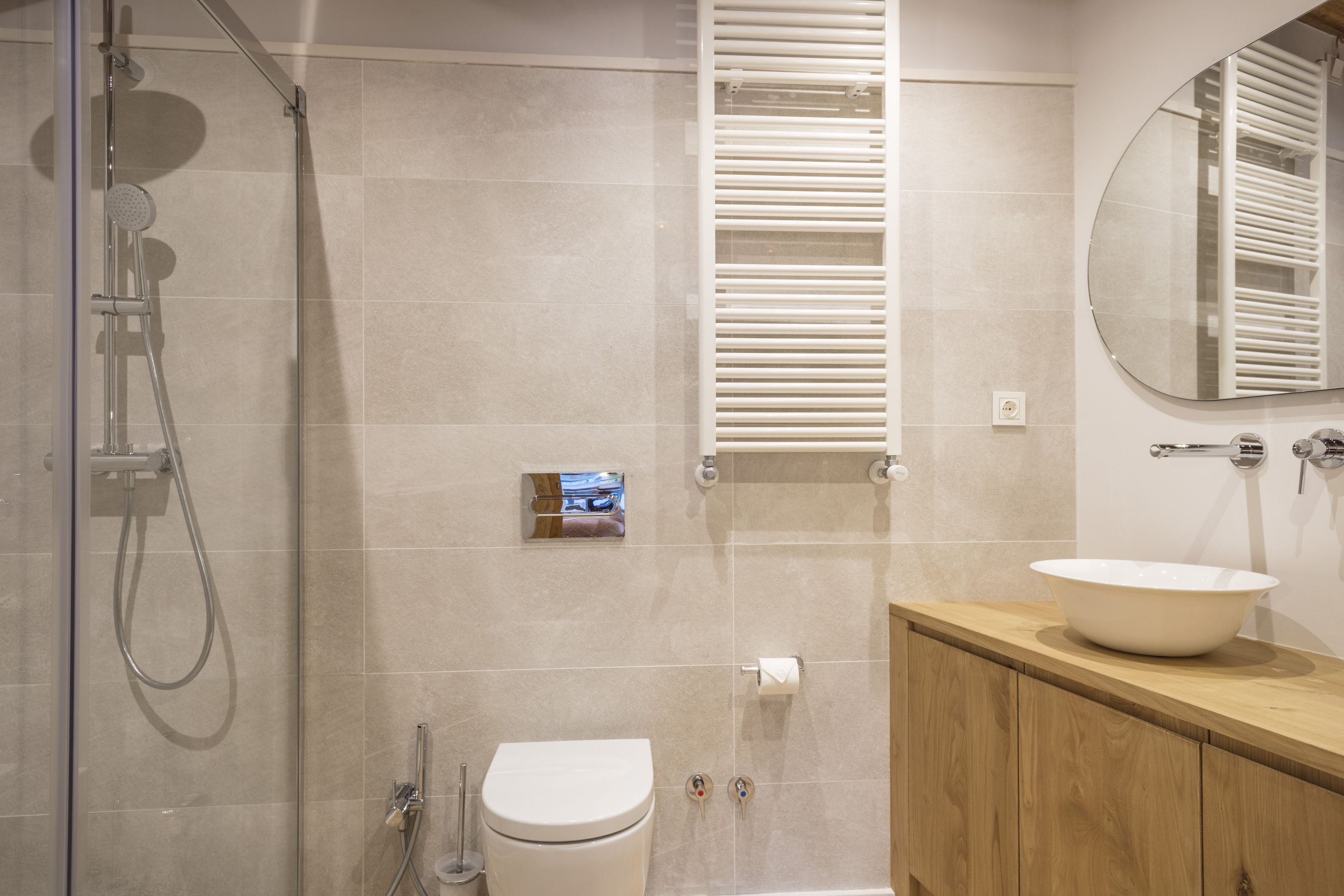 Une salle de bain moderne avec une douche à parois de verre, des toilettes blanches, un meuble-lavabo en bois doté d’un grand évier et un miroir au-dessus de l’évier.
