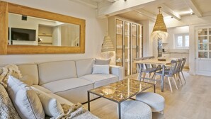 Un vaste espace de vie comprenant un canapé, une table basse et une table à manger avec des chaises. Un grand miroir orne le mur, et un luminaire suspendu éclaire la pièce.