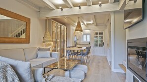 Un grand espace de vie comprenant un canapé, un pouf et une table à manger avec des chaises. Il y a également une cuisine équipée d'une cuisinière et de placards.