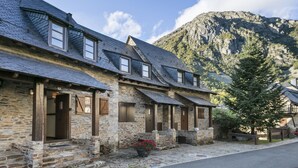 Un bâtiment en pierre, doté d’un toit en pente et de nombreuses fenêtres, situé dans une région montagneuse sous un ciel dégagé.