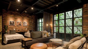 A modern living room with a brick wall, large windows, and a mix of sofas and a bed.