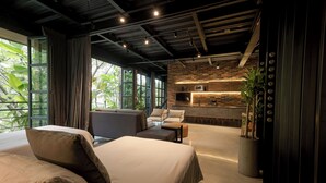 A modern hotel room with a large bed, a sofa, a small table, and a kitchen area.