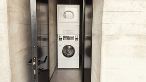 A compact, enclosed laundry room with a stacked washer and dryer, a control panel, and a metal door.