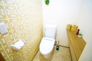 A bathroom with a toilet, a toilet paper holder, a hand dryer, and a small potted plant. - Grande Shagi GS604 (Osaka)