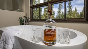 Een badkamer met een wit wastafelmeubel, een fles bourbon whiskey en twee glaasjes.