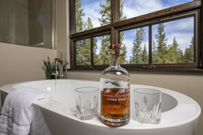 Casa de banho com uma pia branca, uma garrafa de whisky bourbon e dois copos.