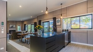 Une cuisine moderne dotée d’un îlot central, de grandes fenêtres et d’un coin repas avec un canapé et une table.