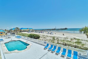 A pool area with lounge chairs, a pier, and a beach.