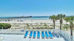 A beach with a pier, sun loungers, and palm trees. - PierWatch I 101 | Oceanfront Six Bedroom Condo (North Myrtle Beach)