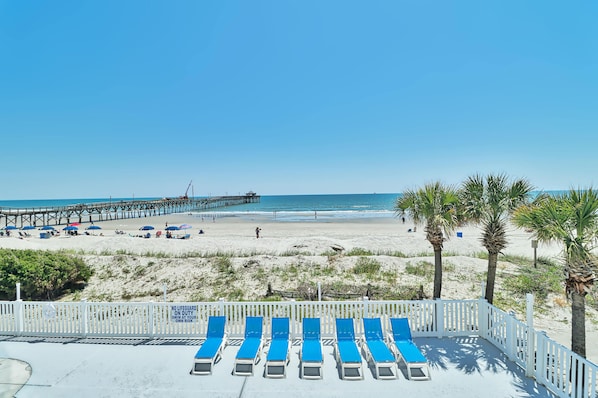 A beach with a pier, sun loungers, and palm trees.