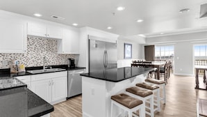 A modern kitchen with white cabinetry, a black countertop, and a stainless steel refrigerator. - PierWatch I 103 | Oceanfront Six Bedroom Condo (North Myrtle Beach)