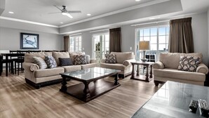 A spacious living room with a large window, a ceiling fan, and a dining area with a table and chairs. - PierWatch I 103 | Oceanfront Six Bedroom Condo (North Myrtle Beach)