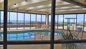 Un espace piscine avec vue sur l’océan, un panneau indiquant la présence d’un sauveteur et un autre panneau signalant une zone peu profonde.