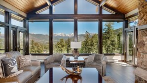 A modern living room with a large window offering a mountain view, a fireplace, and a cozy seating area. - Hyler Mountain Lodge Vacation Home at Windcliff (Estes Park)