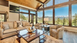 A spacious living room with large windows, a wooden ceiling, and a modern fireplace. - Hyler Mountain Lodge Vacation Home at Windcliff (Estes Park)