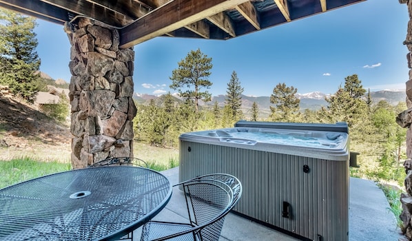 A hot tub under a wooden pergola with a mountain view.
