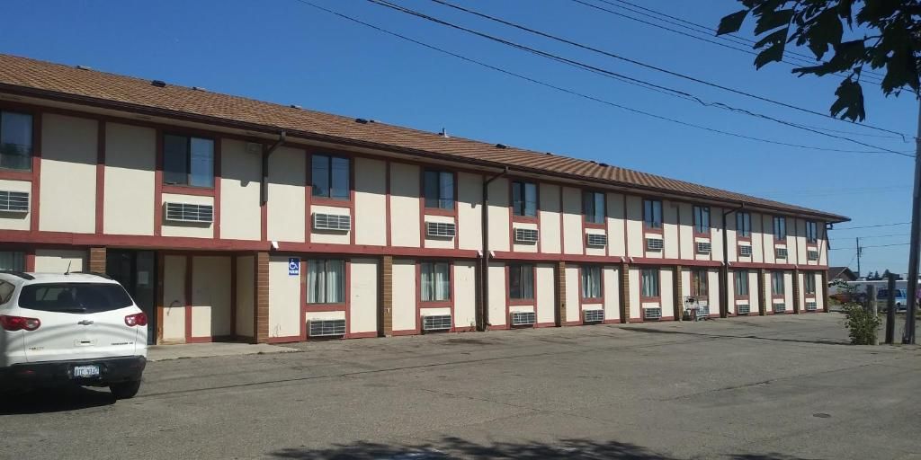 A multi-story motel with a row of rooms, a parking lot, and a white car parked in front.