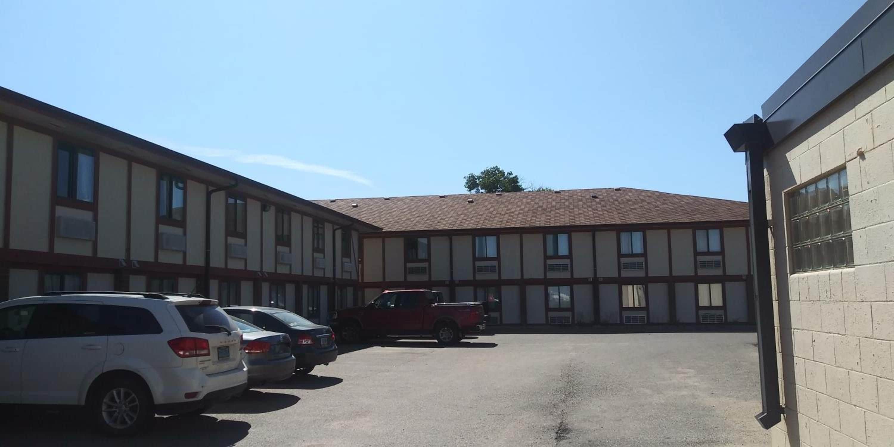A parking area with several cars parked in front of a building with multiple windows and a tiled roof.