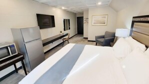 A hotel room with a bed, a desk, a TV, a refrigerator, and a chair. - Guest Lodge (Minot)