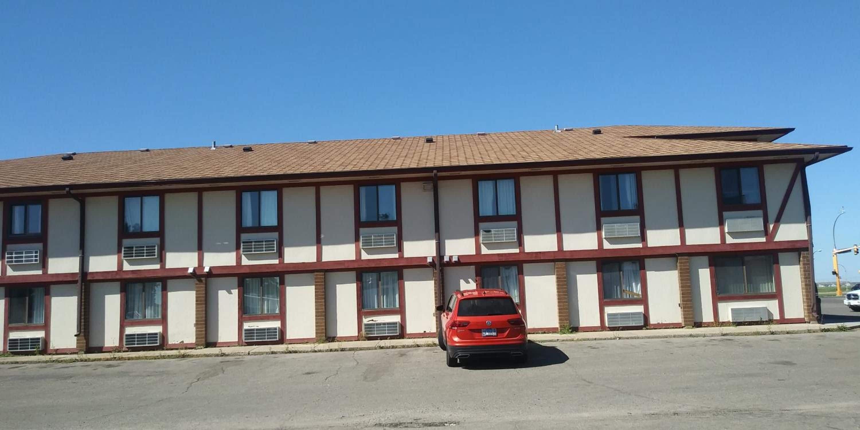 A two-story building with a flat roof, multiple windows, and a red car parked in front.