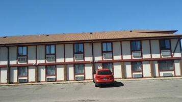 A two-story building with a flat roof, multiple windows, and a red car parked in front.