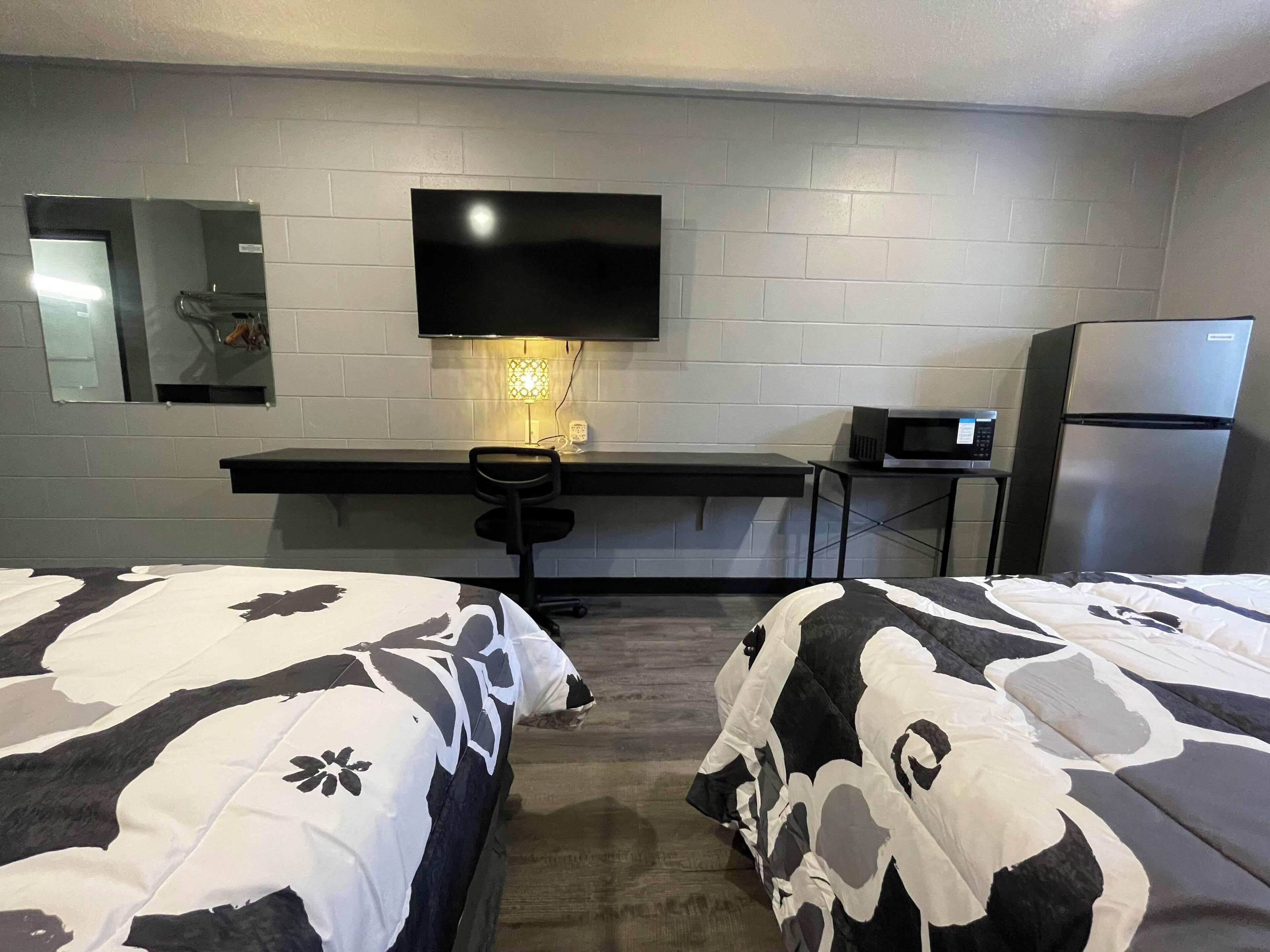 A hotel room with two beds, a desk, a TV, a microwave, and a refrigerator.