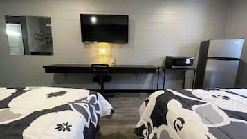 A hotel room with two beds, a desk, a TV, a microwave, and a refrigerator.