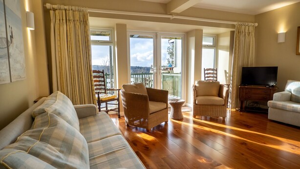 A spacious living room with a wooden floor, a sofa, two armchairs, a television, and a balcony with curtains. - Cottage 360 - Clifden - sleeps 6 guests  in 3 bedrooms (Clifden)
