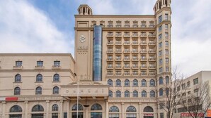 Un hotel de varios pisos con una imponente torre de cristal, varios balcones y una fachada tradicional.