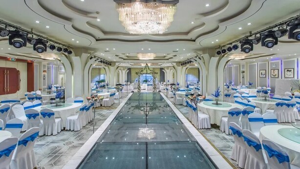 Un salón de banquetes con mesas redondas, manteles blancos y cintas azules.