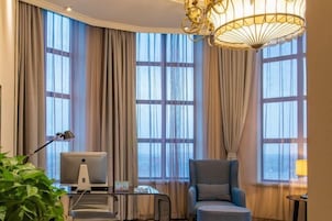 Habitación de hotel con escritorio, computadora, silla y ventanas grandes con cortinas.