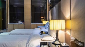 Una habitación de hotel moderna con cama, mesita de noche, lámpara y ventana con vistas.