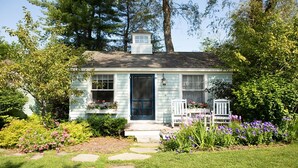 A light blue house with a dark blue door, white windows, and a small porch with white chairs. - SWEET DREAMS COTTAGE (Kennebunkport)