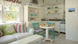 A cozy kitchen with white cabinetry, a dining table, and chairs. There is a window with curtains, a stove, and a sink. - SWEET DREAMS COTTAGE (Kennebunkport)