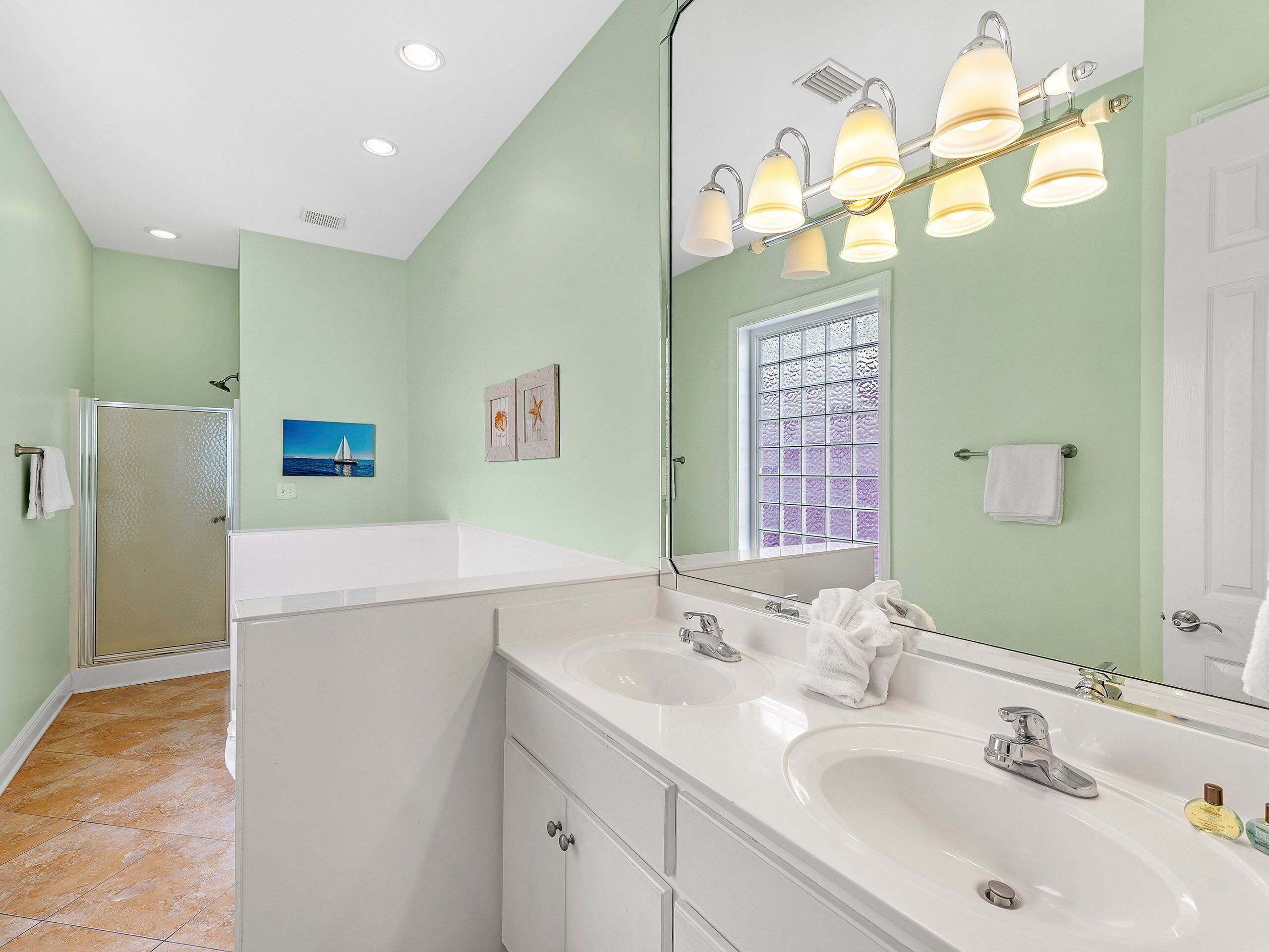 A bathroom with two sinks, a glass shower enclosure, a window with decorative glass, and a painting on the wall.