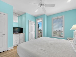 A bedroom with a large bed, a ceiling fan, a TV on a dresser, and a window with blinds.
