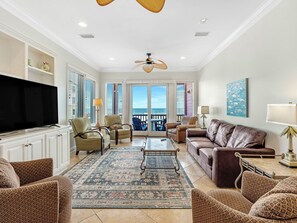 A spacious living room with a large flat-screen TV, comfortable seating, a ceiling fan, and a view to the outside. - Sarah's Beach Baby, East Unit. Beachfront. Pool! Sleeps 24. Gulf Shores! (Gulf Shores)