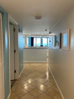 A hallway with a tiled floor, a door on the left, and a view of a balcony with a railing. - OCEANFRONT 3BD-3B Condo - ground floor. (Daytona Beach)