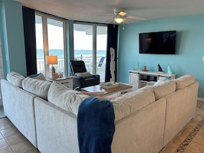 A living room with a sofa, a chair, a coffee table, a TV, and a view of the ocean. - OCEANFRONT 3BD-3B Condo - ground floor. (Daytona Beach)