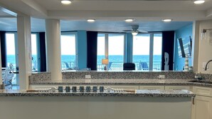 Tilava keittiö, jossa on suuri keittiösaareke, merinäköala ja parveke, jossa on ulkotilaa istuimineen.