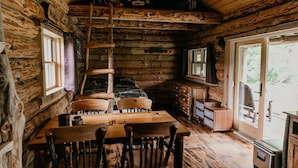 Een rustiek houten interieur met een eettafel, stoelen, een open haard en een groot raam.