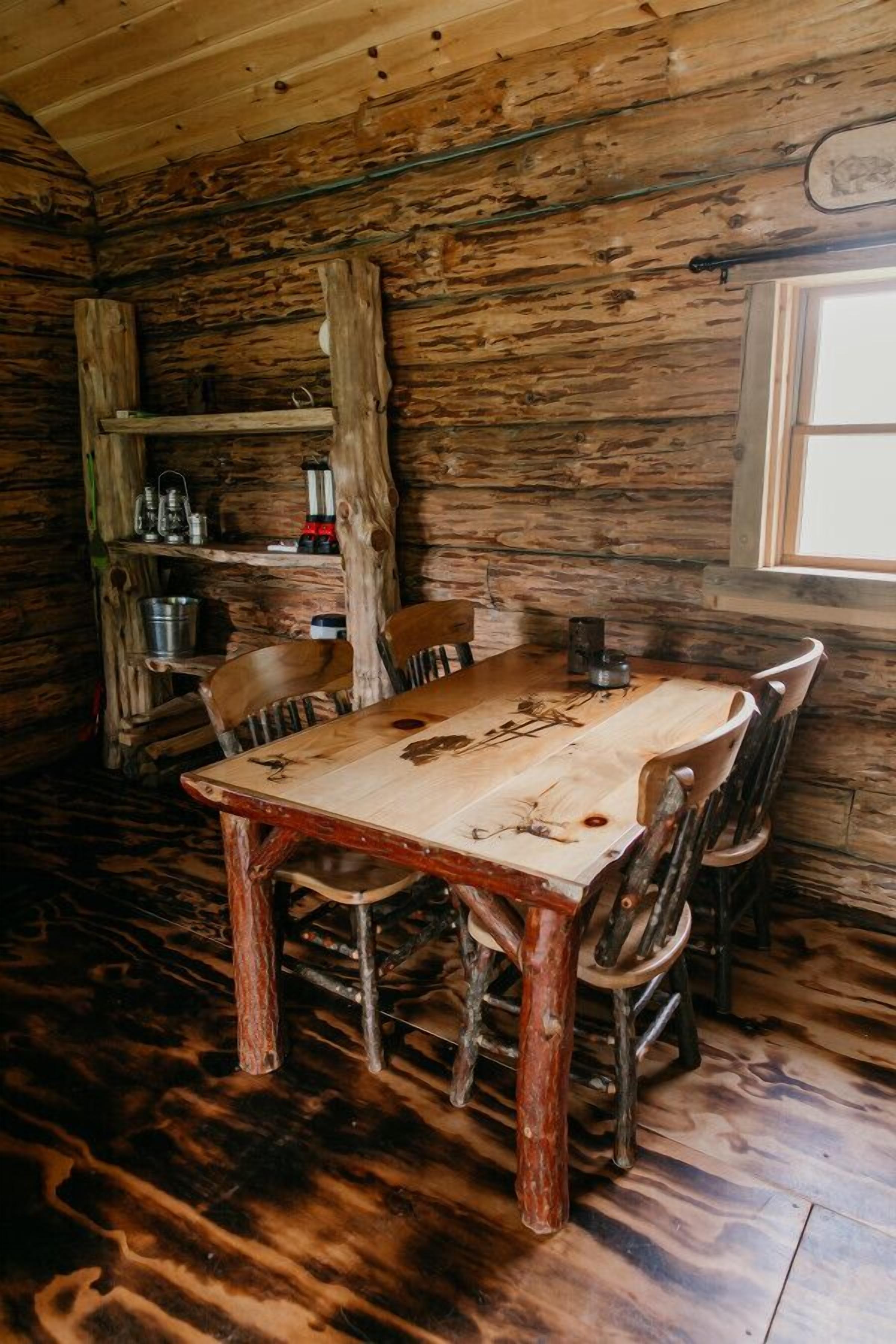 Une table à manger en bois rustique, avec des chaises, une étagère contenant divers objets et une fenêtre.