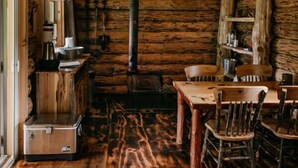Een rustiek houten interieur met een houten plafond, een centraal rookkanaal, een eettafel met stoelen en een klein keukentje.