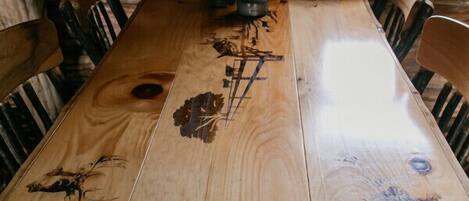 Ein rustikaler Holztisch mit geschnitzten Verzierungen, umgeben von Holzstühlen, vor einer Holzwand mit einem Fenster darüber.