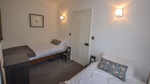 A small, clean room with two single beds, a desk, and two wall-mounted lamps.