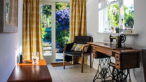 A room with a sewing machine on a wooden table, a chair with a cushion, and a window with curtains.